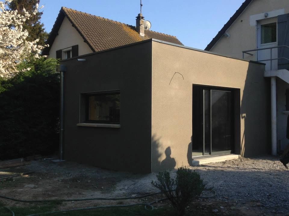 Extension de maison à toit plat, façade enduite taupe et baie vitrée coulissante à cadre sombre